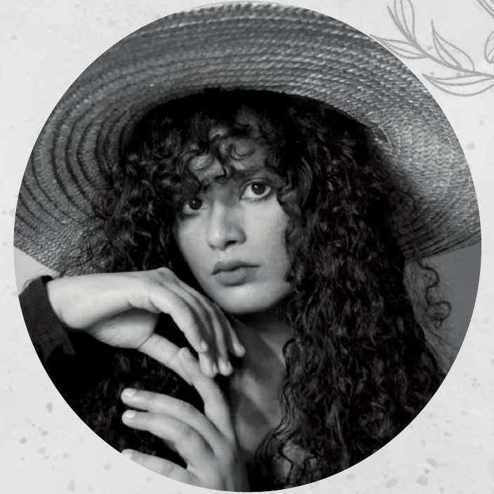 Black and white portrait of Falguni Joshi in a wide-brimmed straw hat, curly hair falling over her shoulder