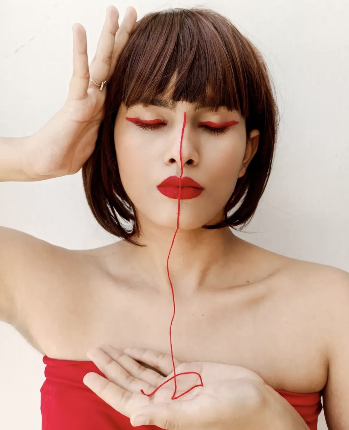 Self portrait, eyes closed: the red thread runs down the centre of the face and ends in a loose knot resting in an open palm