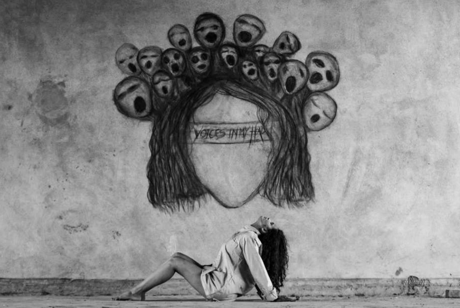 The artist seated beneath her charcoal wall mural of hair fanning into a crown of screaming faces